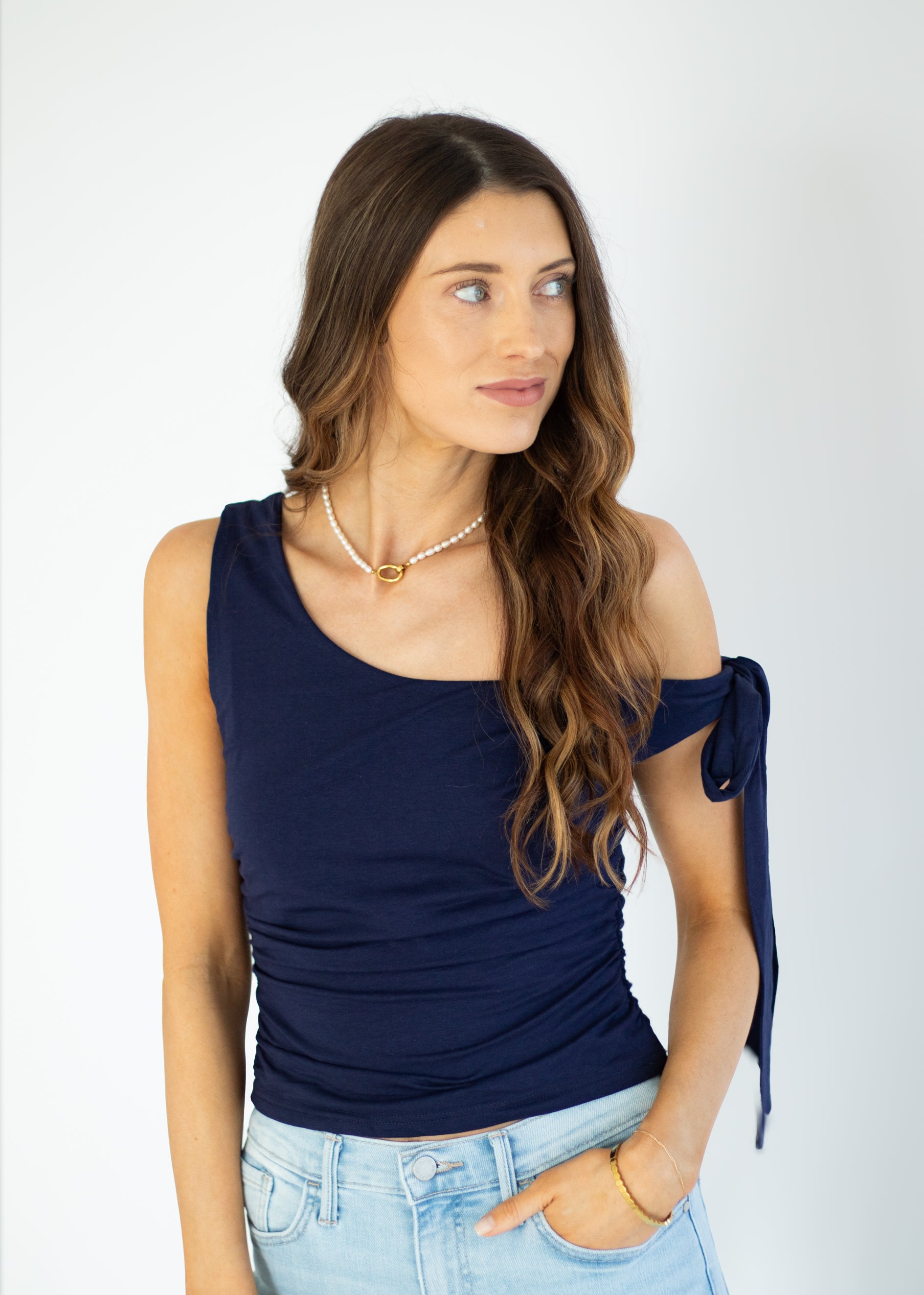 Woman wearing a navy blue sleeveless top with a bow detail on a white background