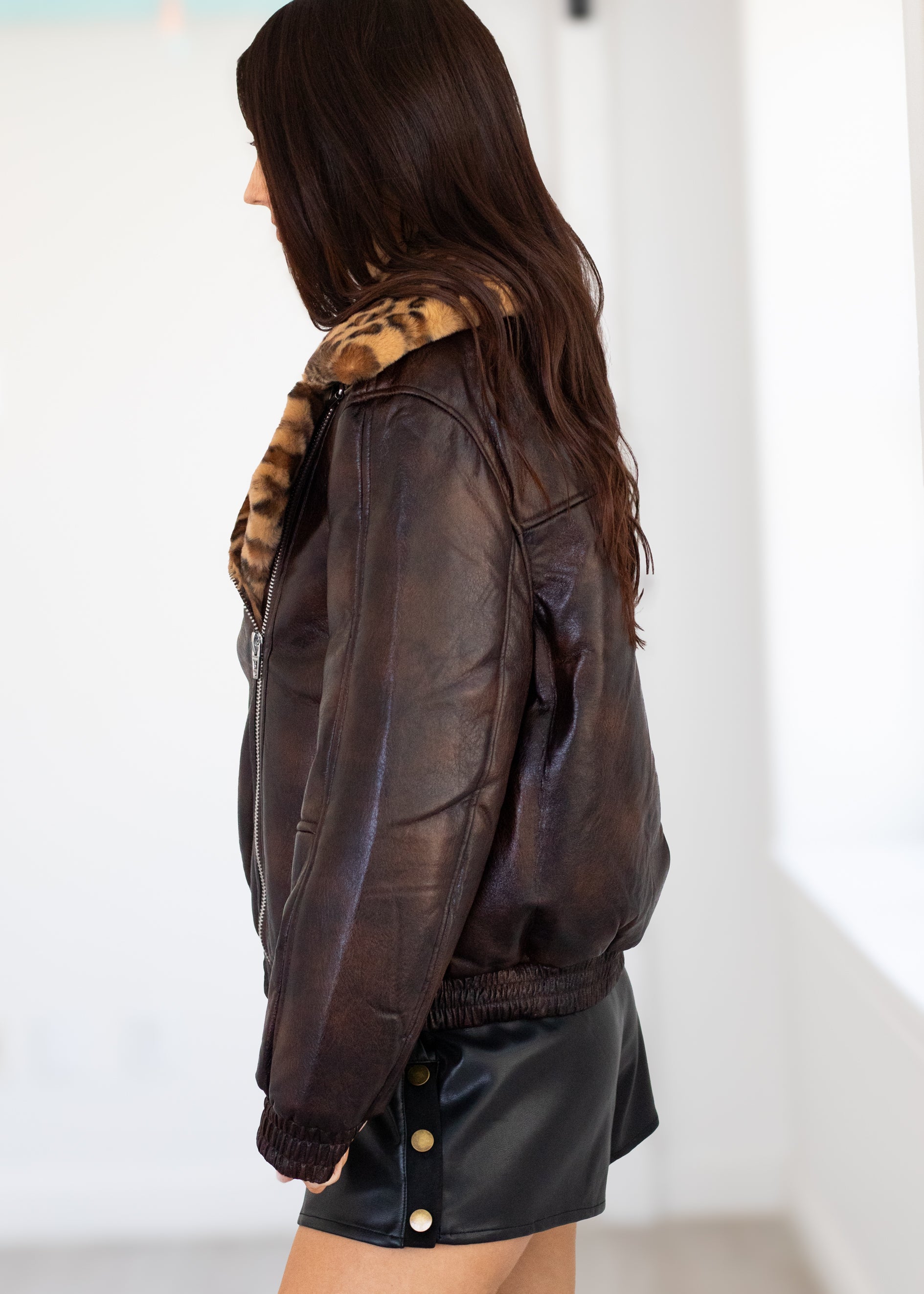 Person wearing a brown leather jacket with a leopard print fur collar on a white background