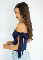 Woman wearing a navy off-shoulder top with a bow detail on a white background