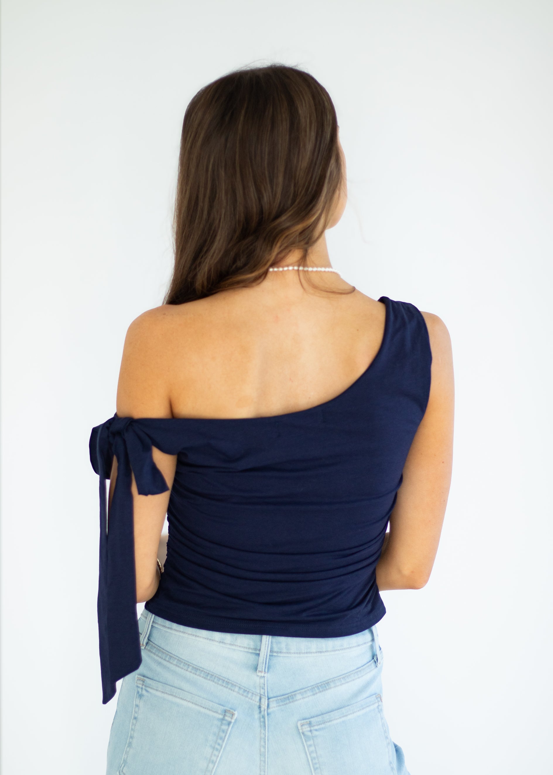 Woman wearing a navy one-shoulder top and light blue jeans on a white background