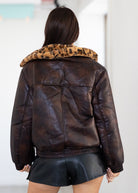 Brown leather jacket with leopard print collar worn by a person on a white background