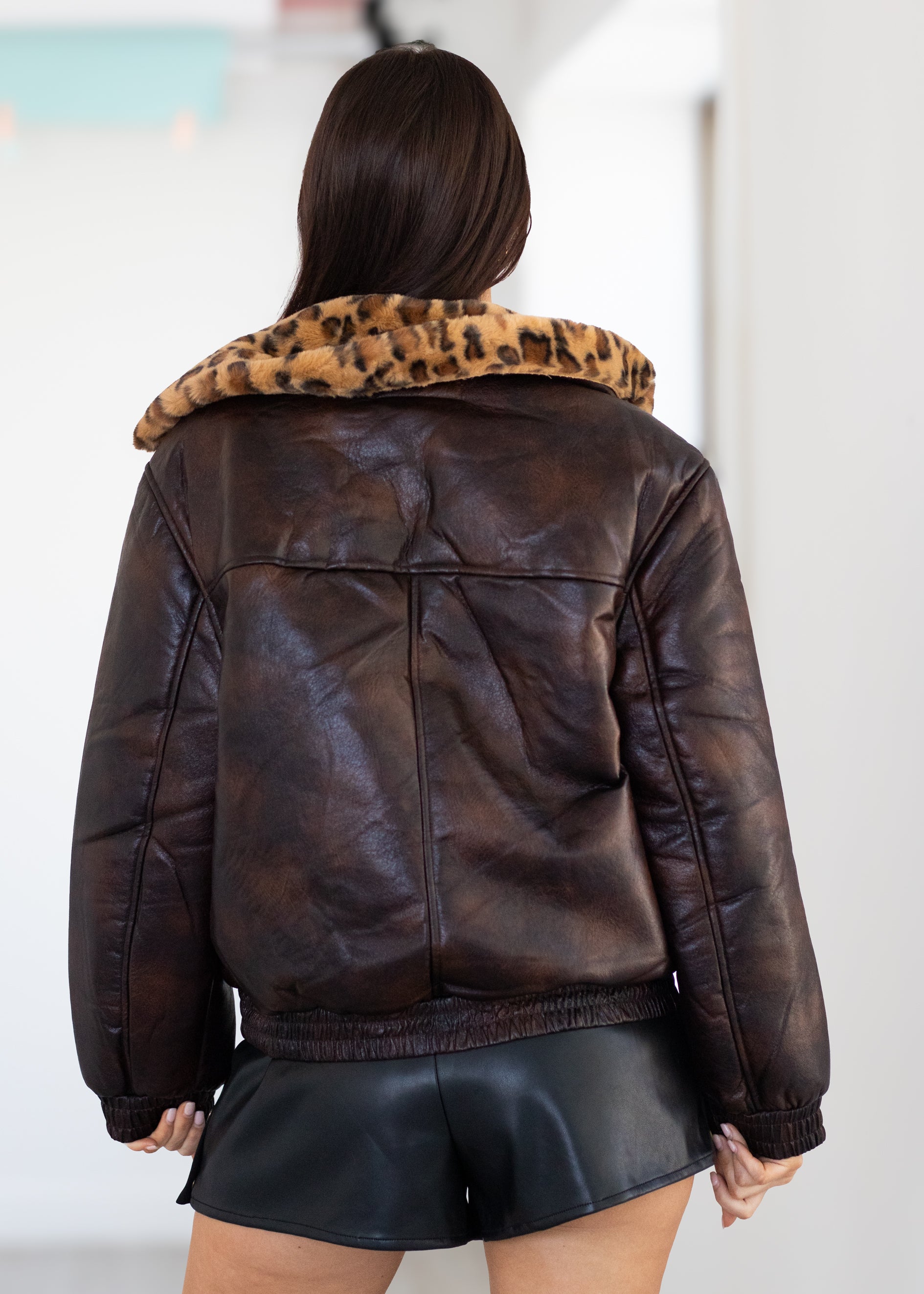 Brown leather jacket with leopard print collar worn by a person on a white background