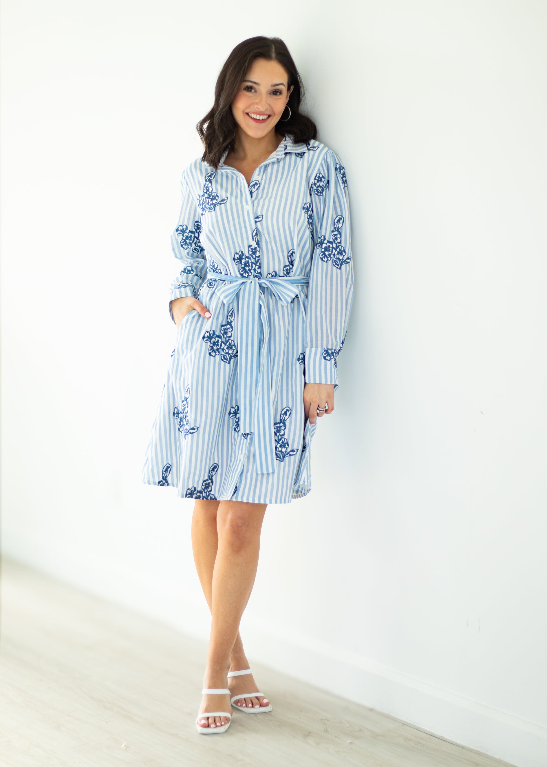 Woman wearing a blue and white striped dress with floral patterns against a white background