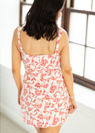 Woman wearing a floral dress with red and white pattern in a bright room.