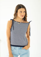 Woman wearing a navy and white striped sleeveless top with light blue jeans on a white background