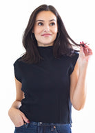 Woman wearing a black sleeveless top and blue jeans on a white background