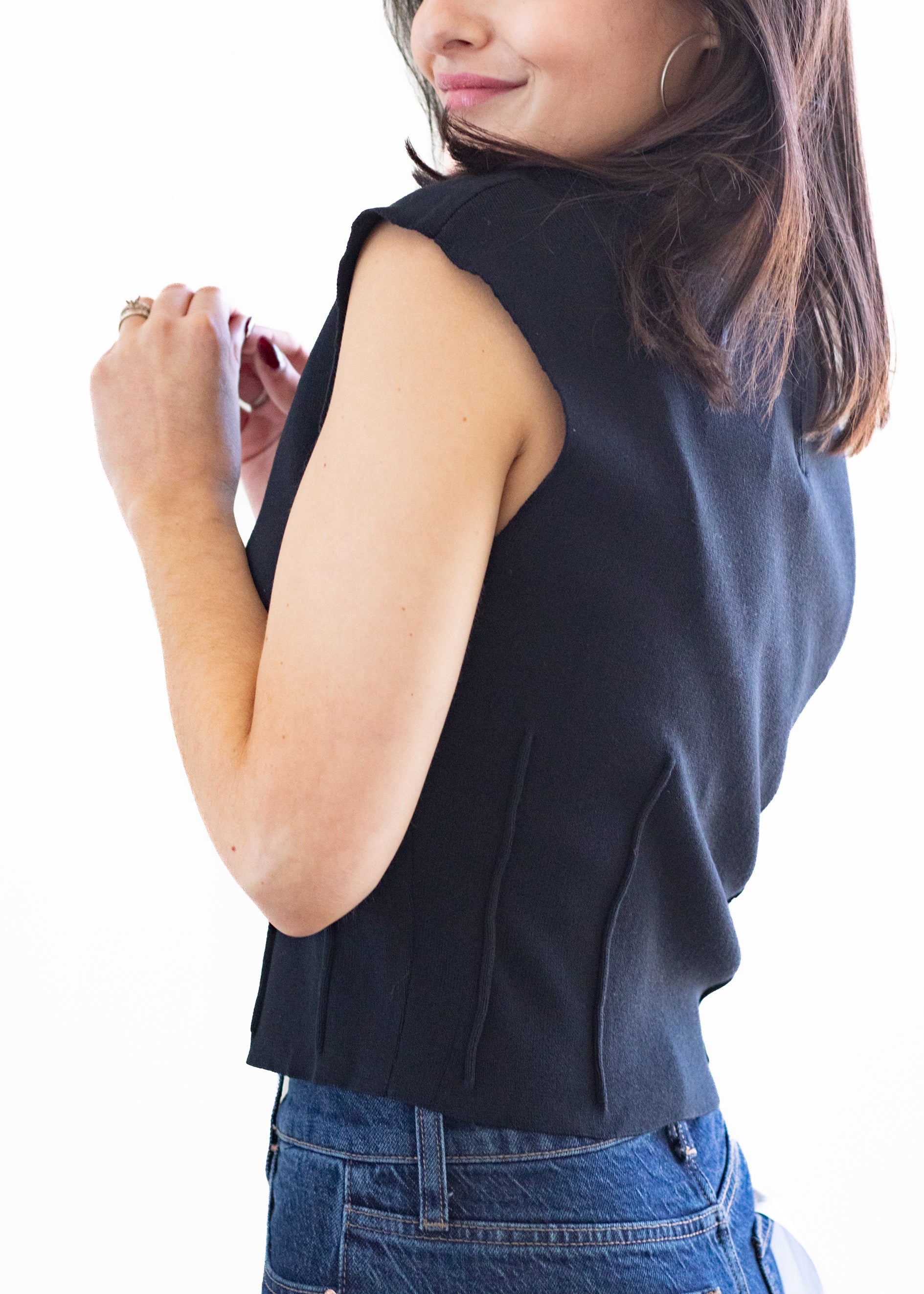 Woman wearing a black sleeveless top and blue jeans on a white background