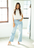 Woman wearing a white blouse and light blue jeans in a bright room.