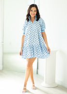 Woman wearing a light blue dress with white polka dots in a minimalistic setting.