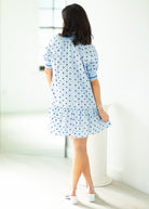 Woman wearing a light blue dress with white polka dots in a minimal indoor setting.