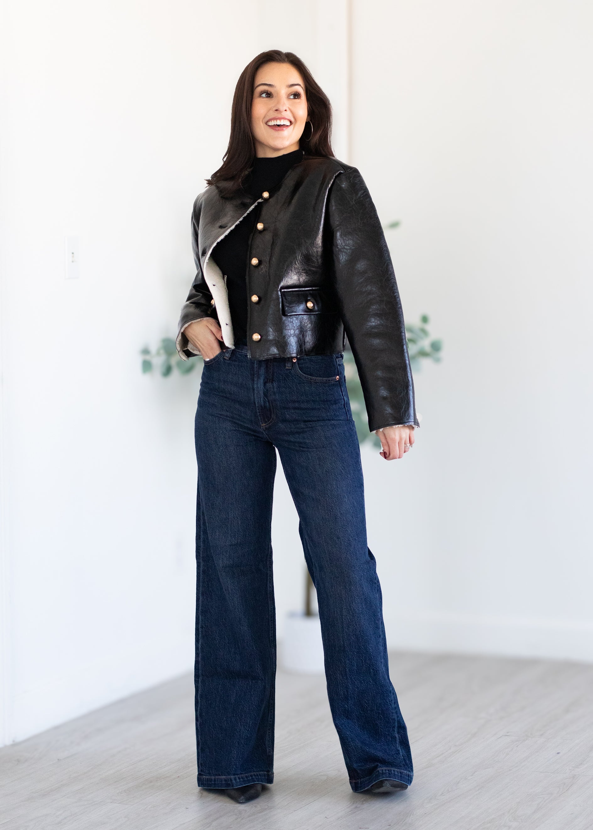 Woman wearing a black leather jacket and blue jeans standing against a white background