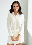 Woman wearing a white shirt dress against a plain background