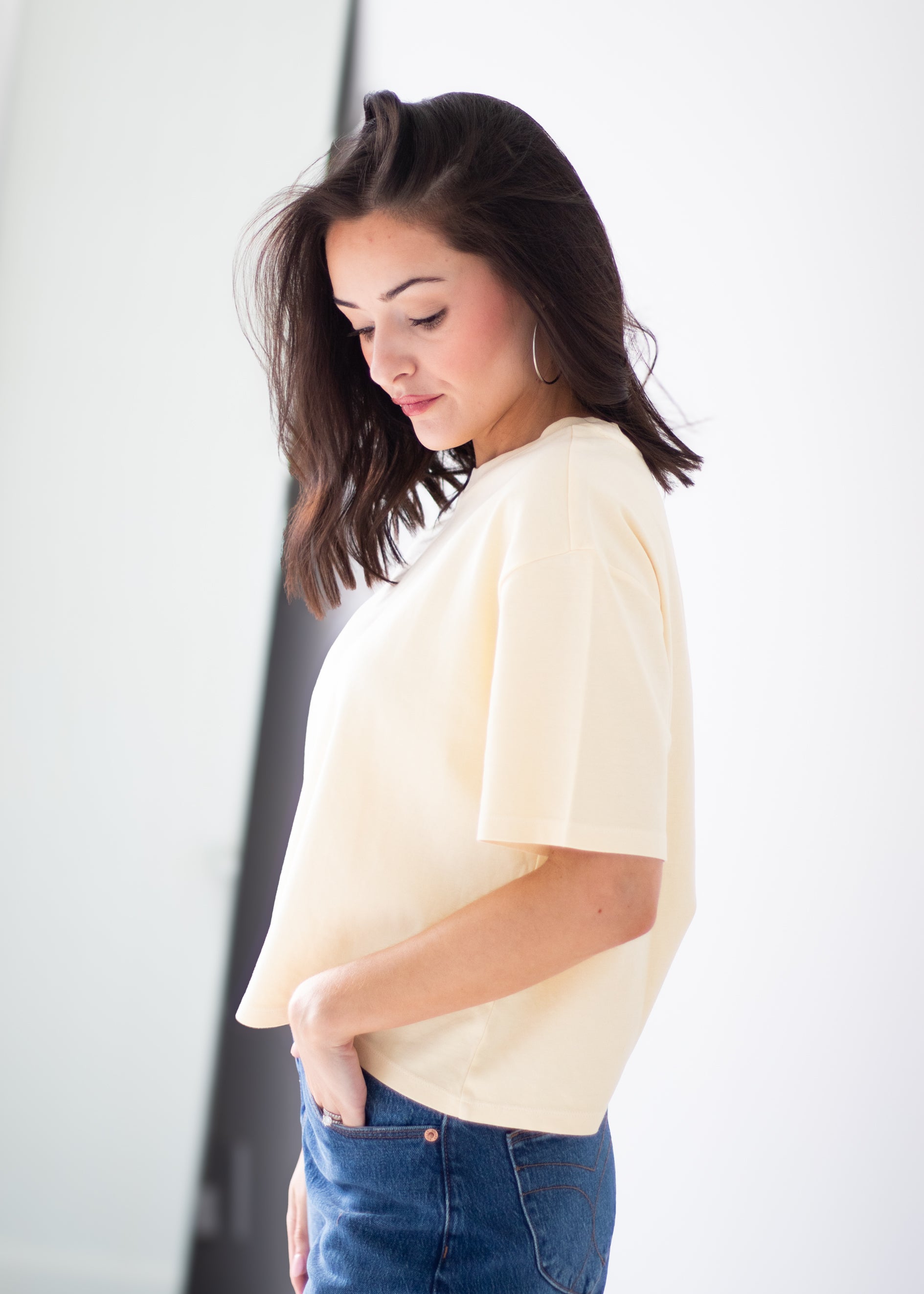 A woman wearing a cream-colored short-sleeve crop top and blue jeans, shown from a side profile against a white background.