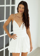 Woman wearing a white dress standing against a white wall.
