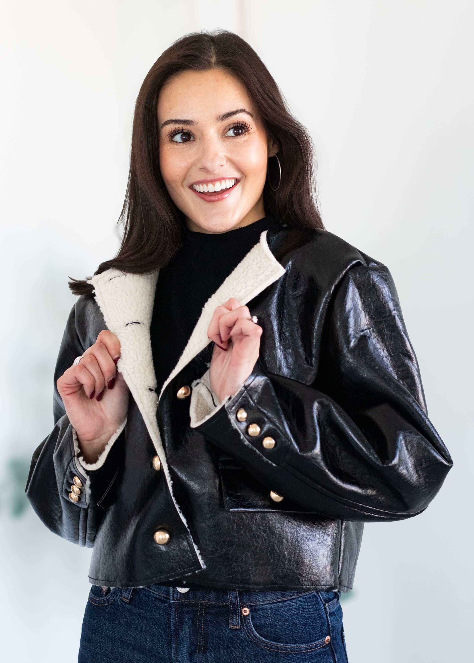 Woman wearing a black leather jacket with a white interior on a plain background