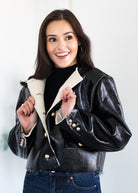 Woman wearing a black leather jacket with a white interior on a plain background