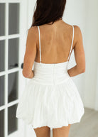 Person wearing a white dress with thin straps in a minimal indoor setting