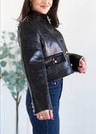 Woman wearing a black leather jacket with gold buttons against a light background