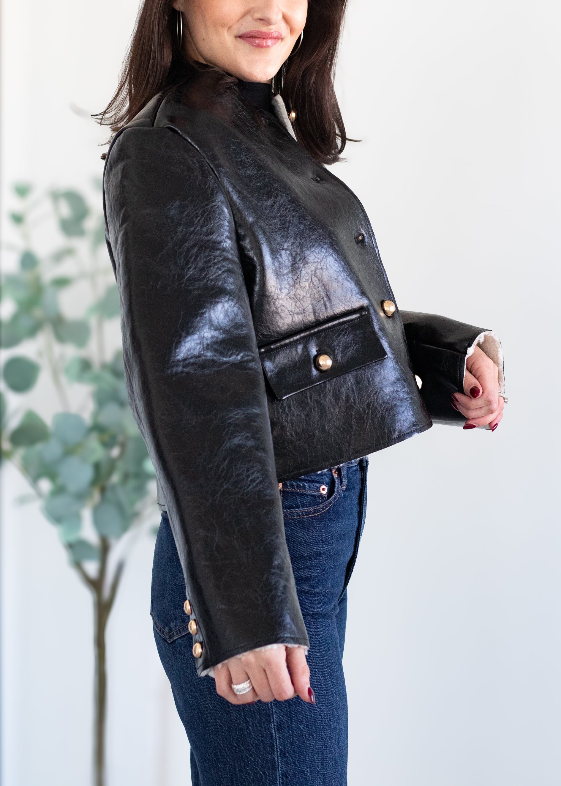 Woman wearing a black leather jacket with gold buttons against a light background