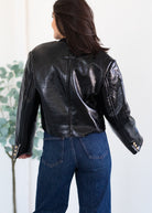 Person wearing a black leather jacket and blue jeans against a white background