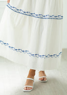 White dress with blue embroidery and white sandals on a light wooden floor