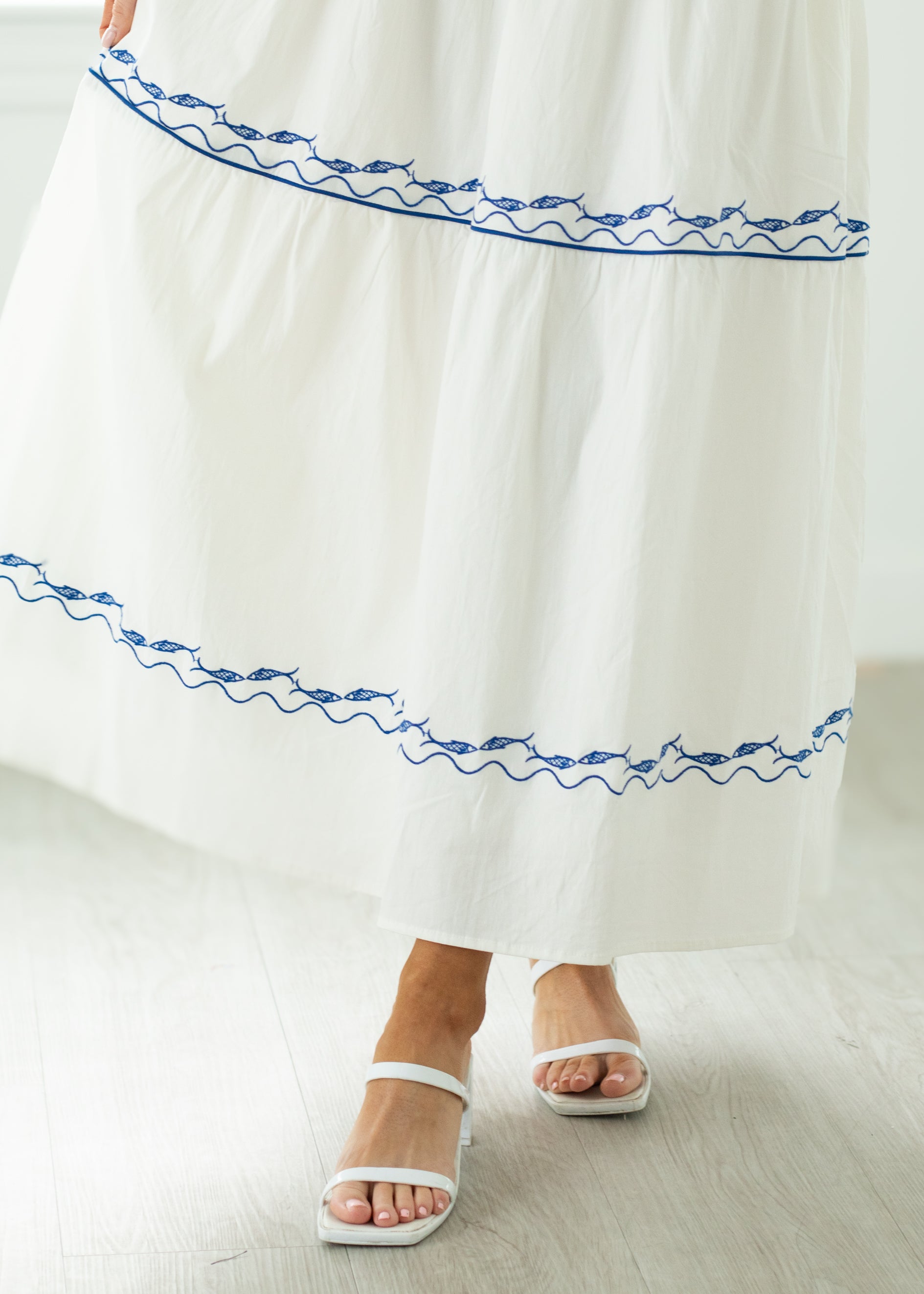 White dress with blue embroidery and white sandals on a light wooden floor