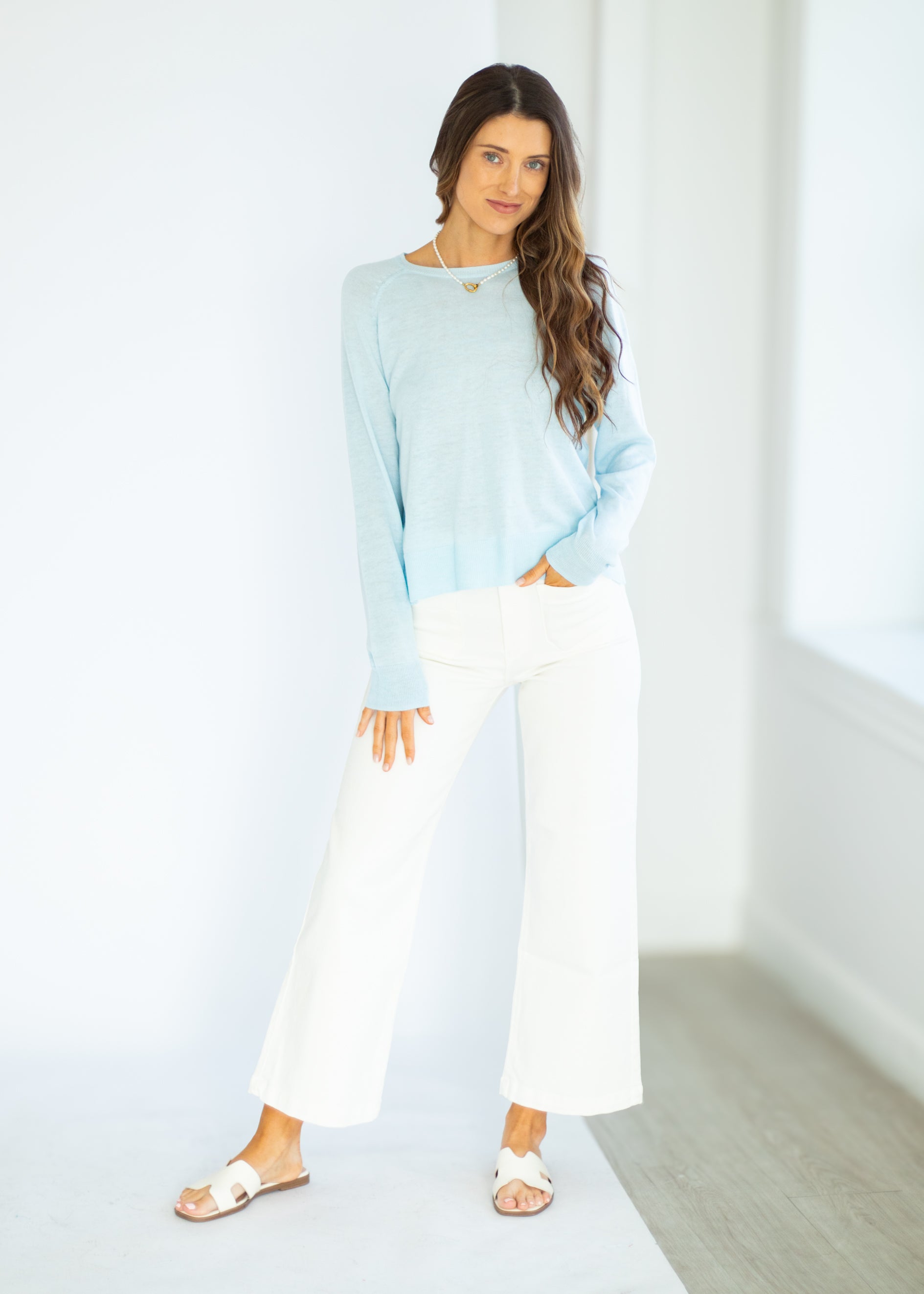 Woman wearing a light blue top and white pants in a minimalistic setting