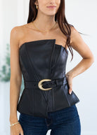Woman wearing a black strapless top with a gold belt and blue jeans against a white background