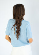 Person wearing a light blue sweater with long hair, standing against a white background