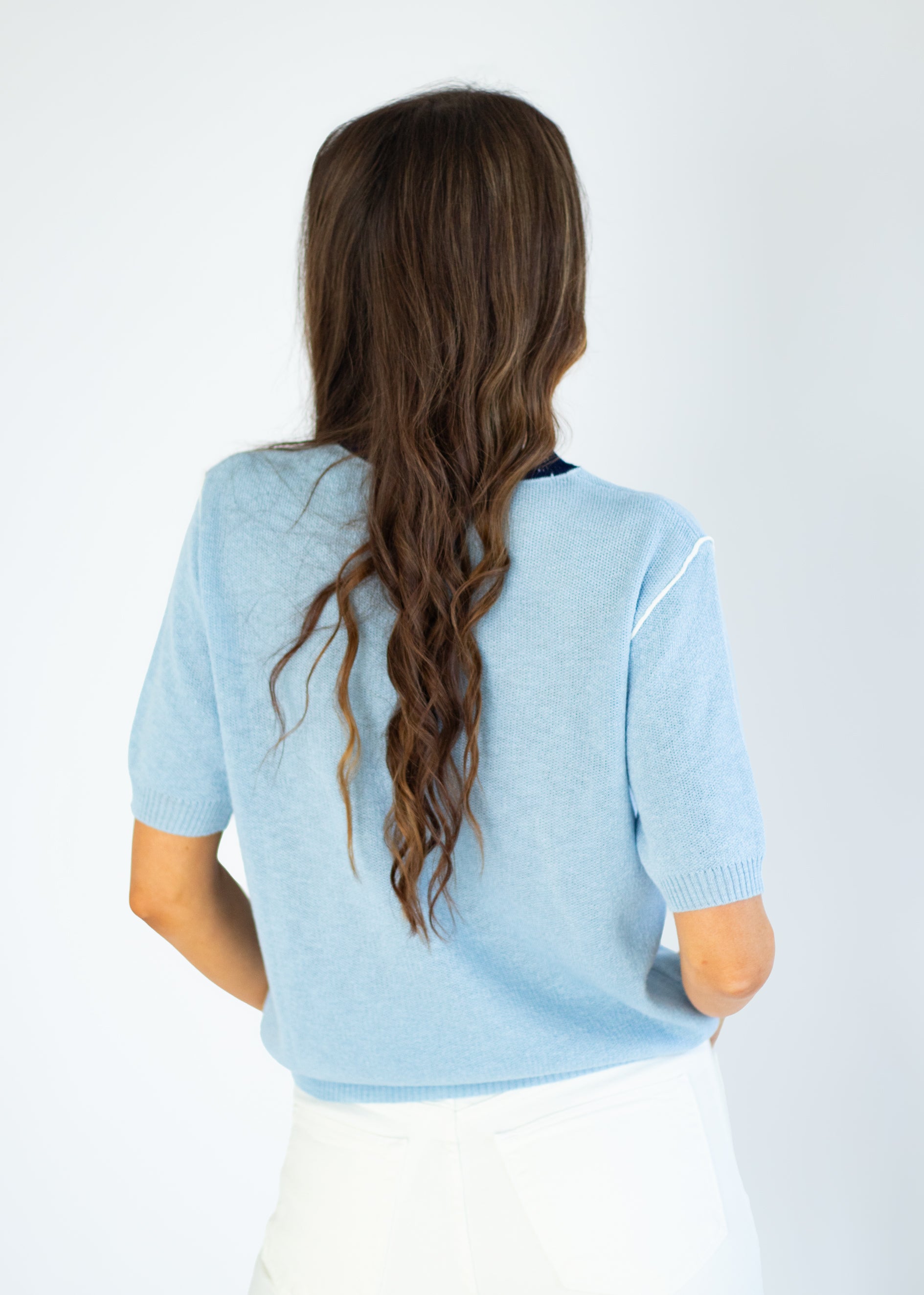 Person wearing a light blue sweater with long hair, standing against a white background