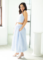 Woman wearing a light blue sleeveless top and wide-leg pants in a bright room.