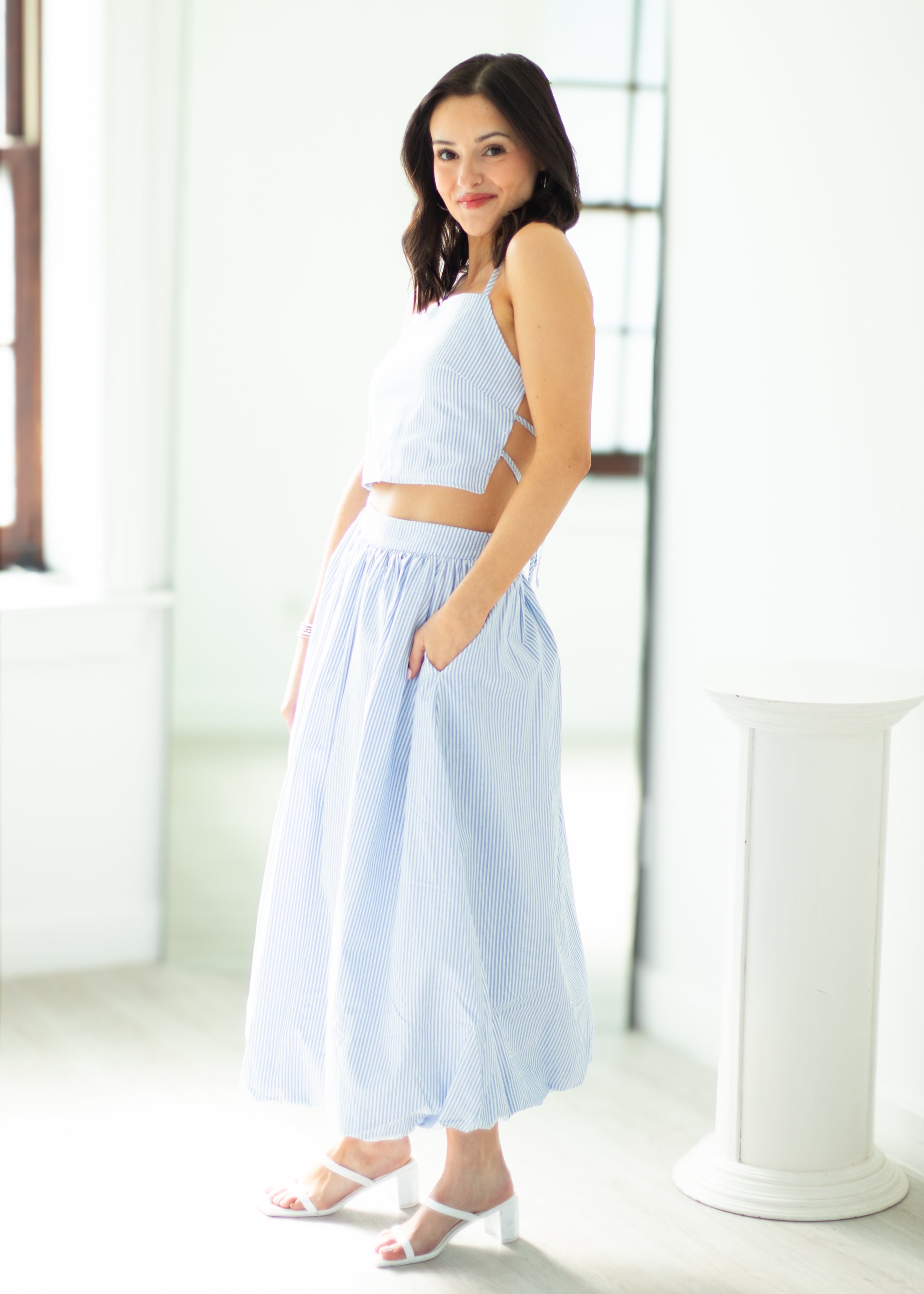 Woman wearing a light blue sleeveless top and wide-leg pants in a bright room.