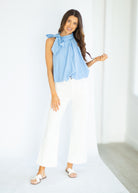 Woman wearing a light blue top with a bow and white pants on a white background