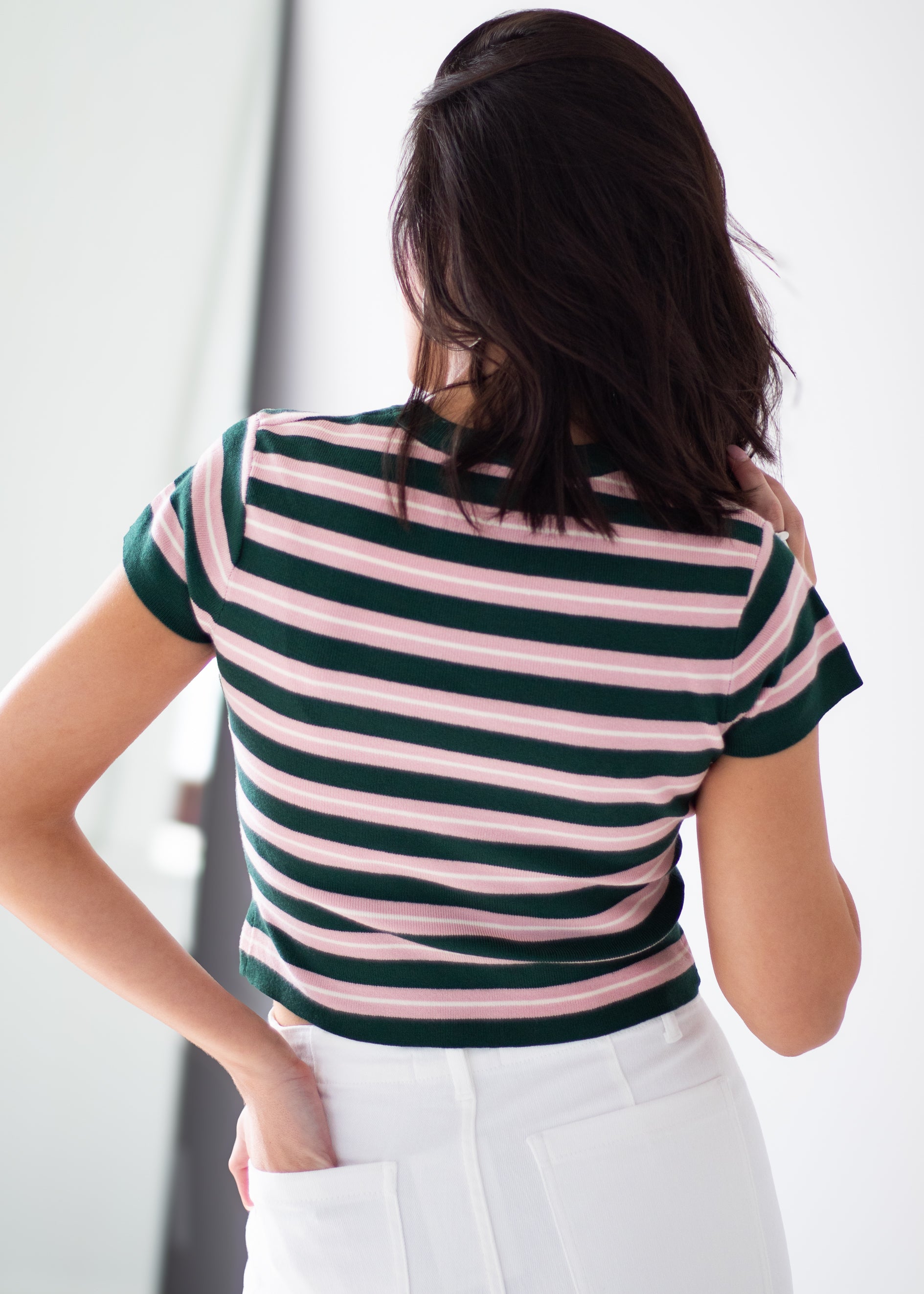 A woman viewed from behind wearing a short-sleeve ribbed top with horizontal dark green and light pink stripes, paired with white pants.