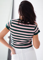 A woman viewed from behind wearing a short-sleeve ribbed top with horizontal dark green and light pink stripes, paired with white pants.