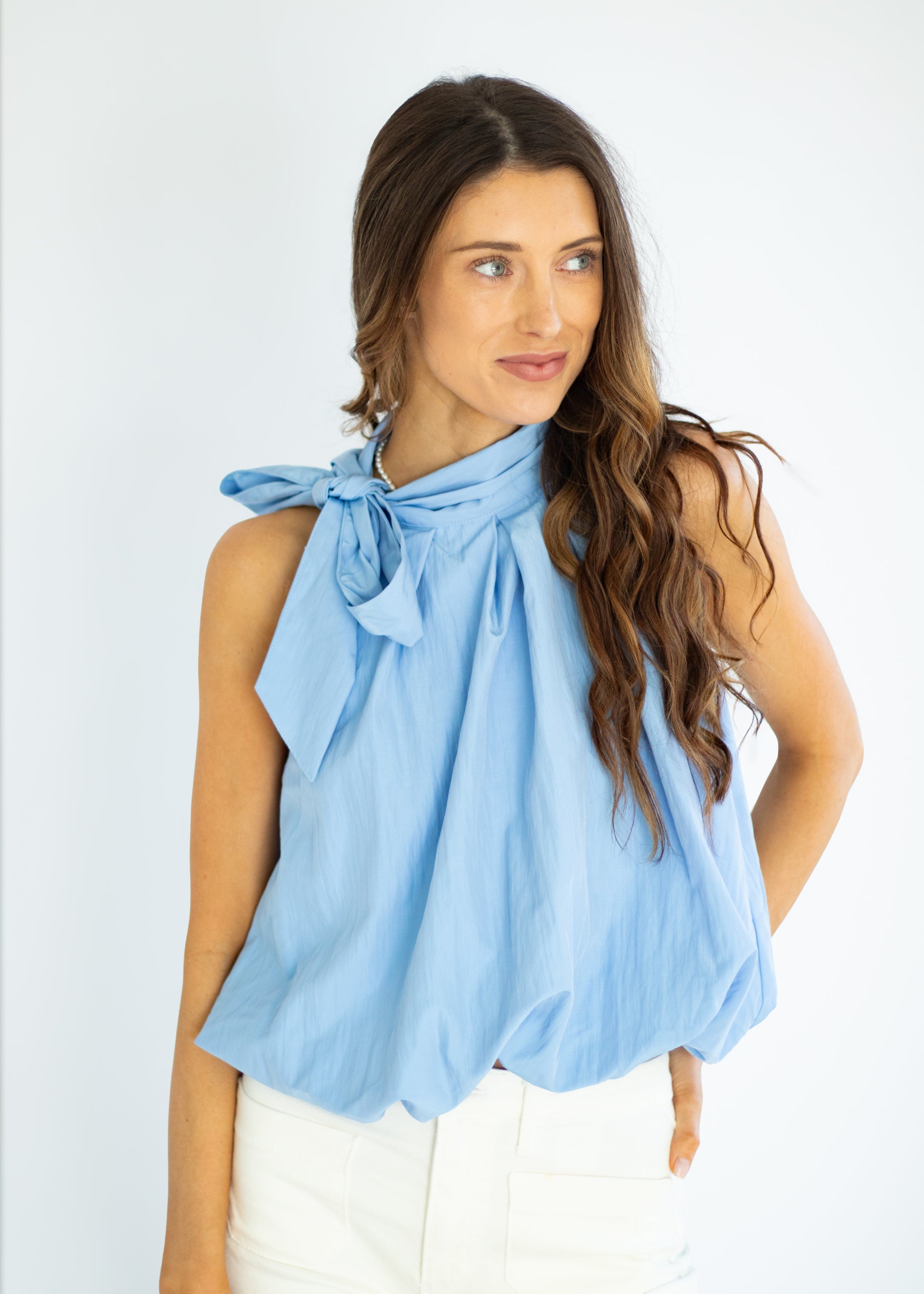 Woman wearing a light blue sleeveless top with a bow detail on a white background