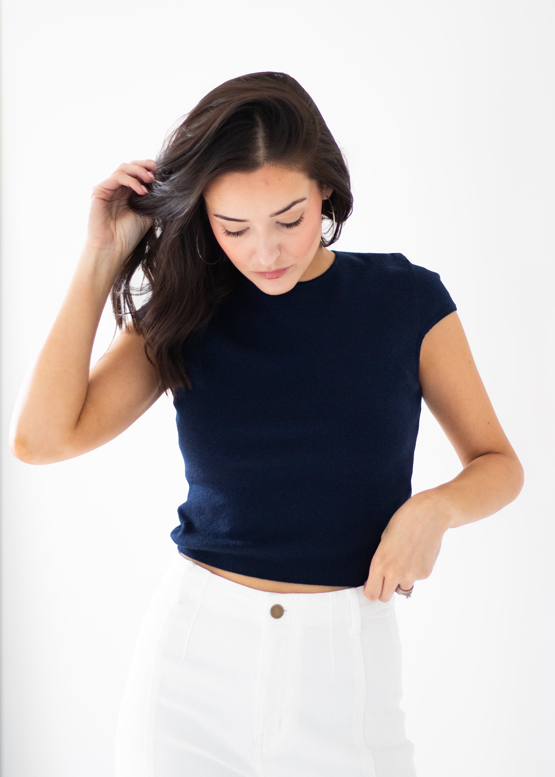 A woman wearing a navy blue short-sleeve knit top and white pants, posing against a clean white background.