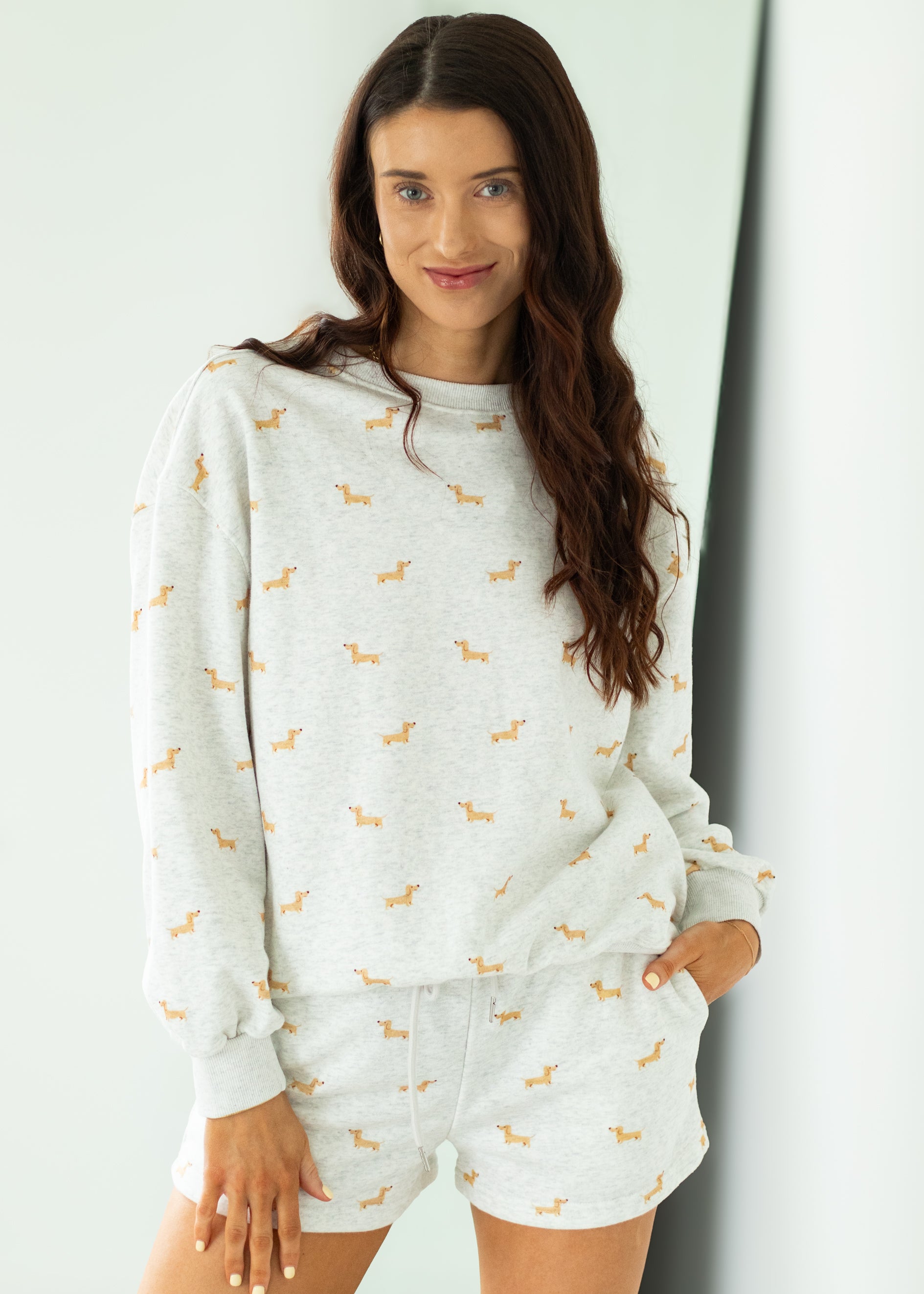 Woman wearing a white sweatshirt and shorts set with small patterns, standing against a light background.