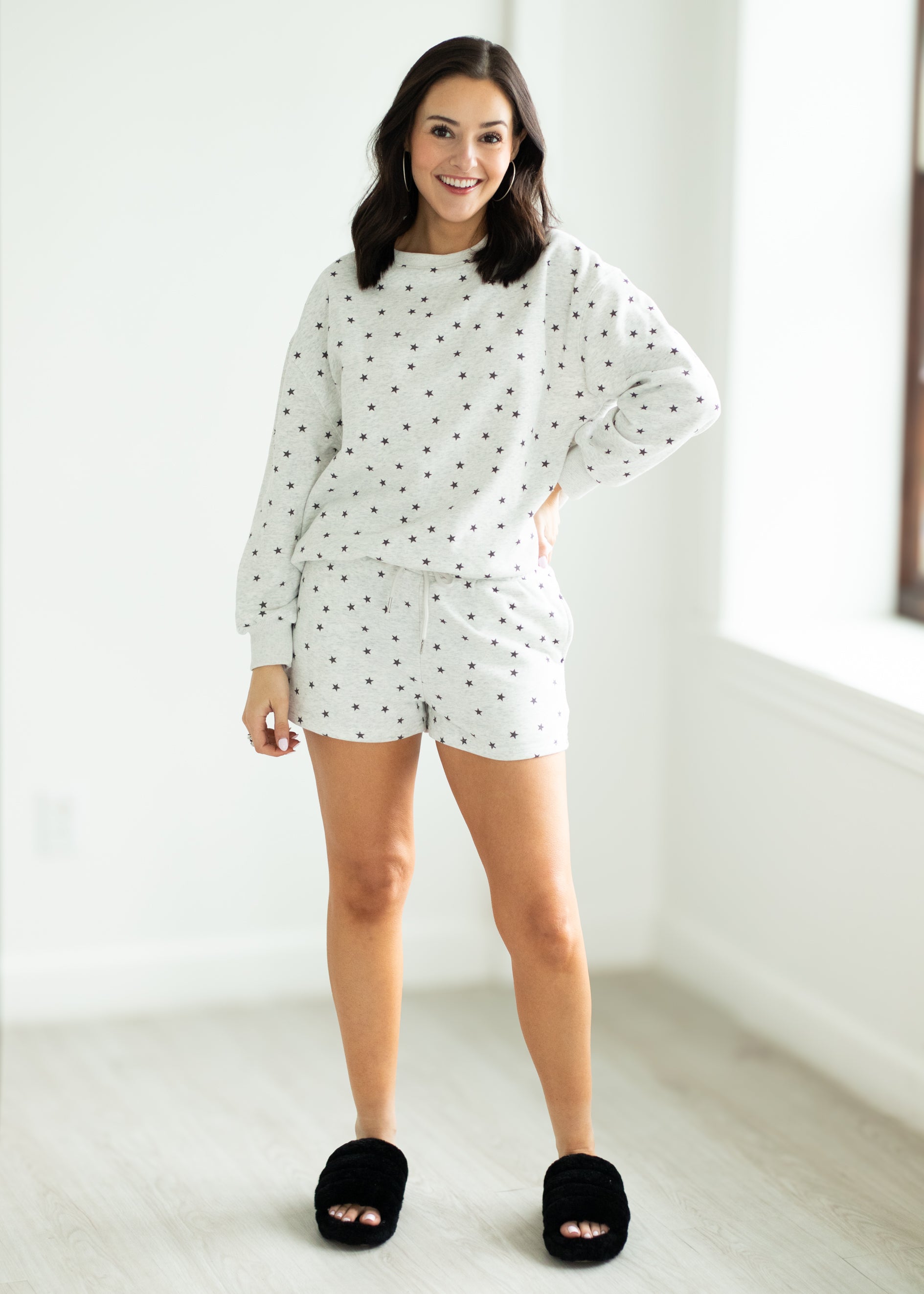 Woman wearing a white outfit with black stars in a minimalistic room.