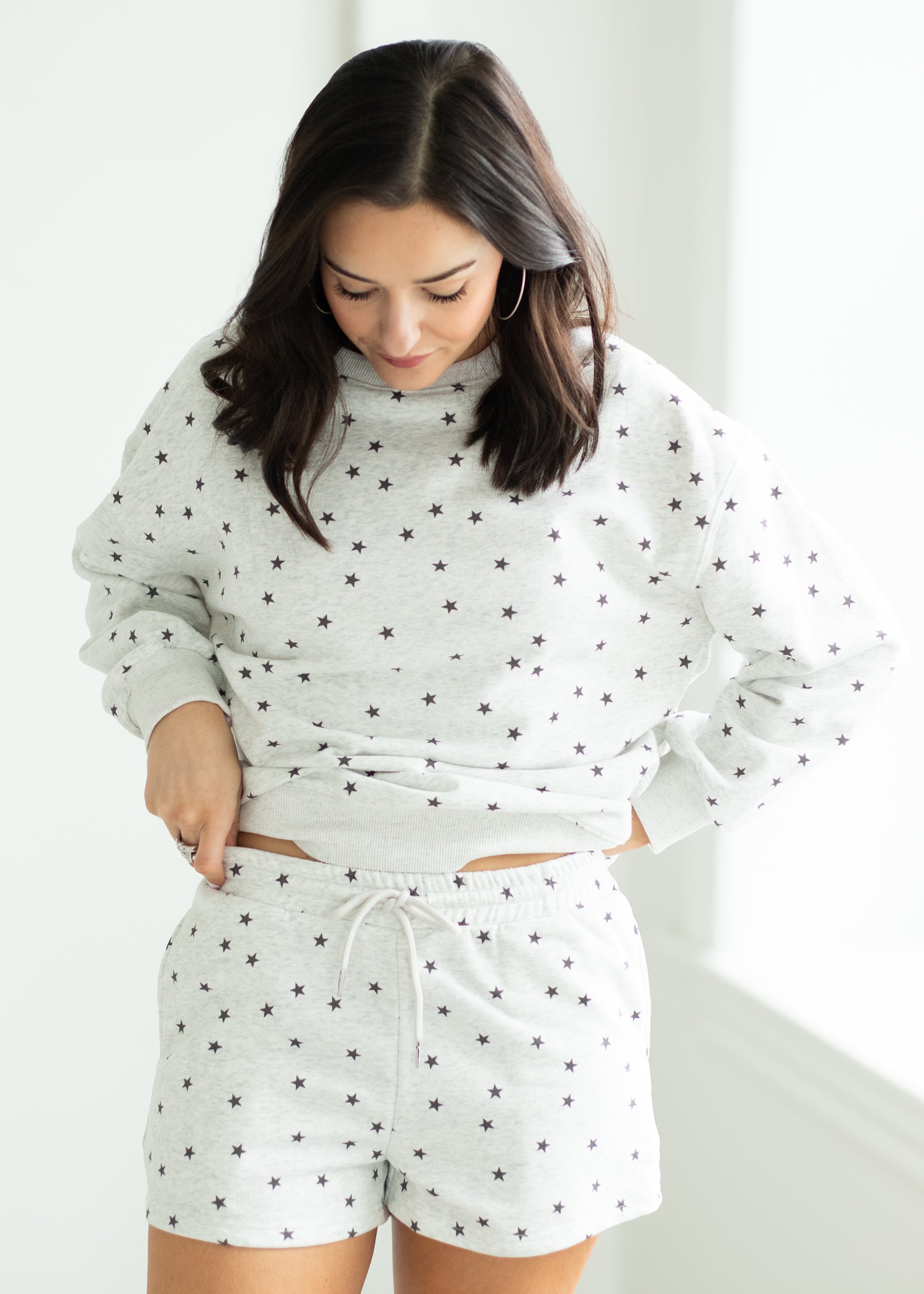 Woman wearing a white outfit with black stars in a minimalistic room.
