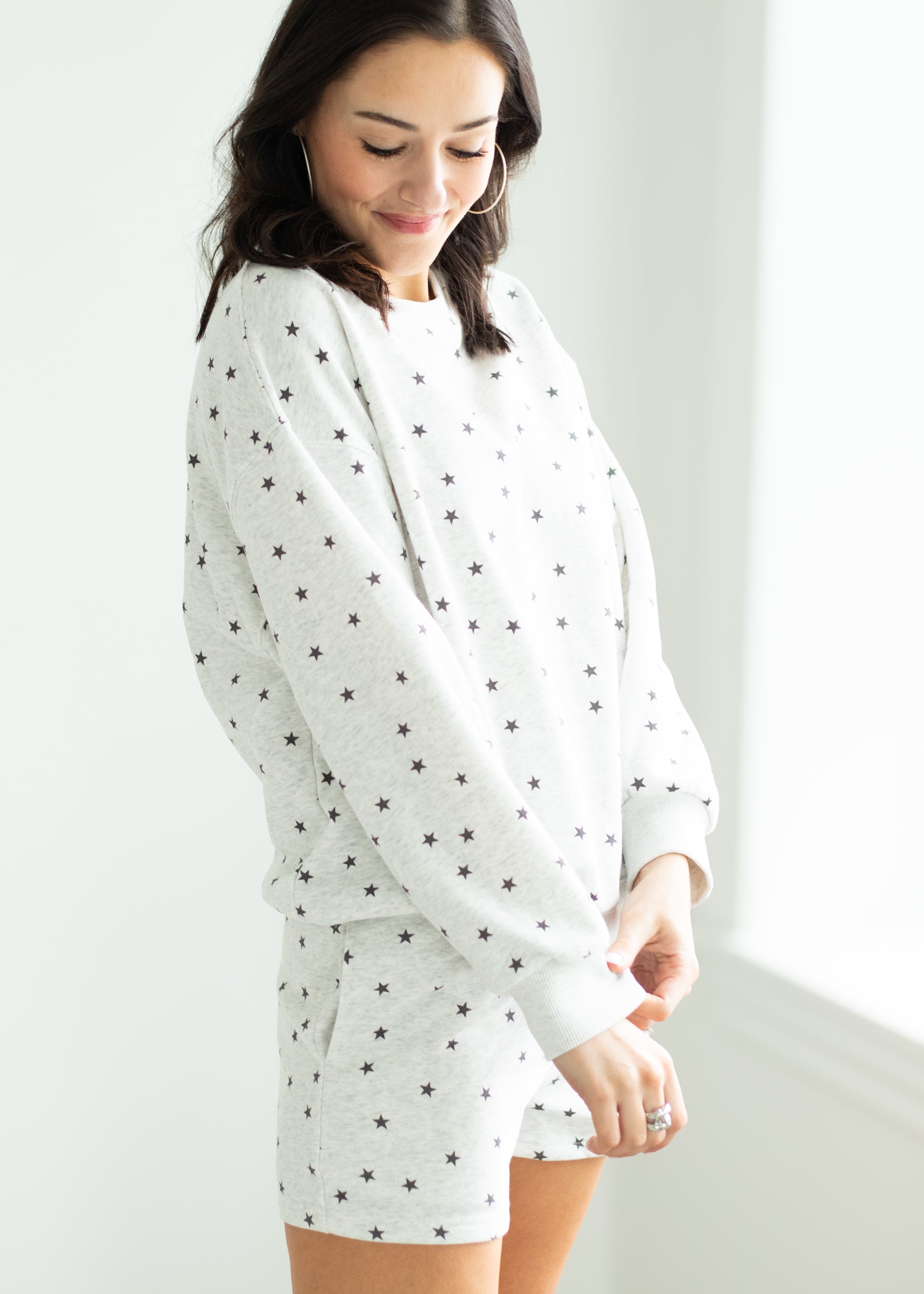 Woman wearing a white outfit with black stars in a minimalistic room.