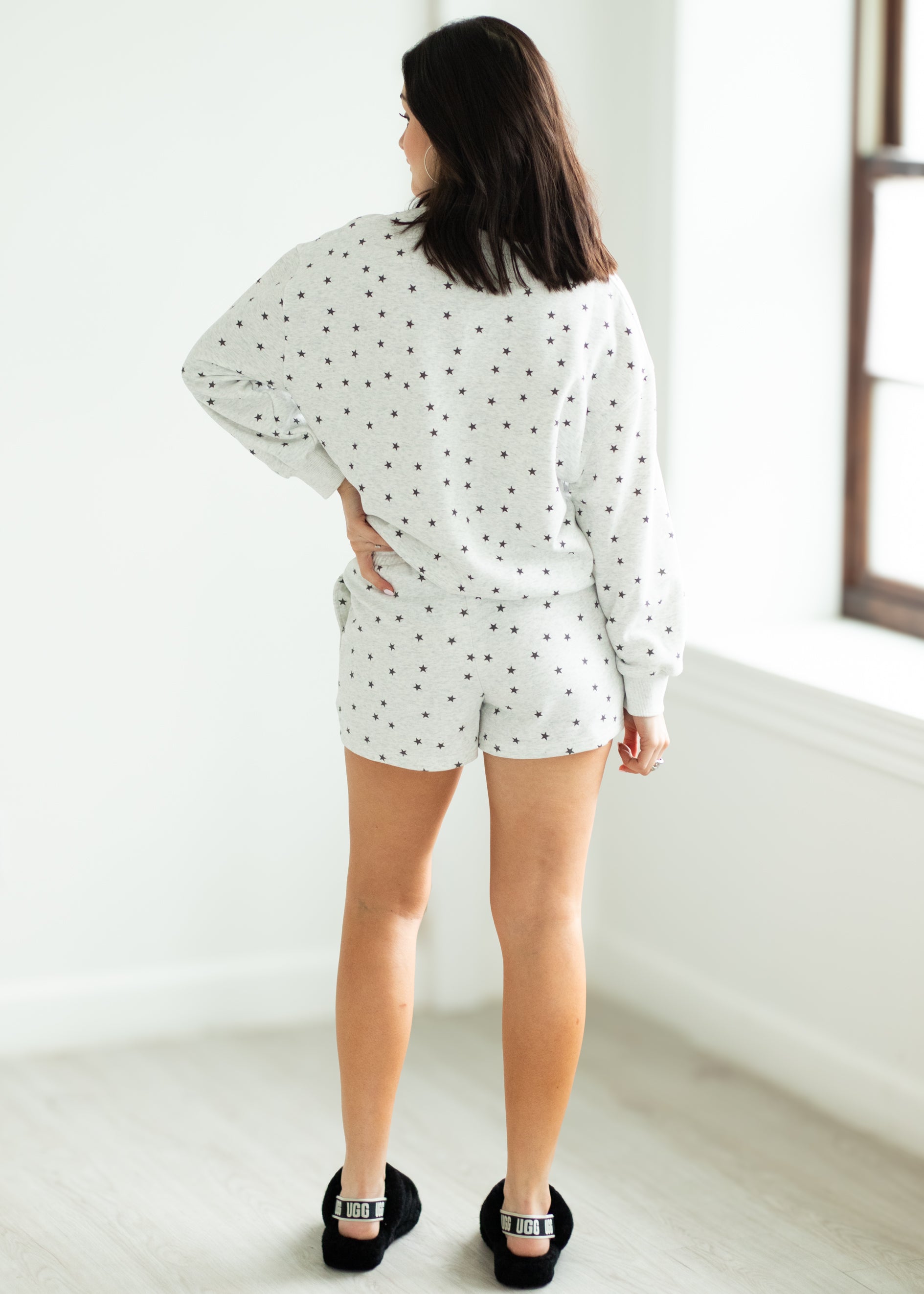 Woman wearing a white outfit with black stars in a minimalistic room.