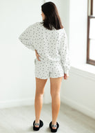 Woman wearing a white outfit with black stars in a minimalistic room.