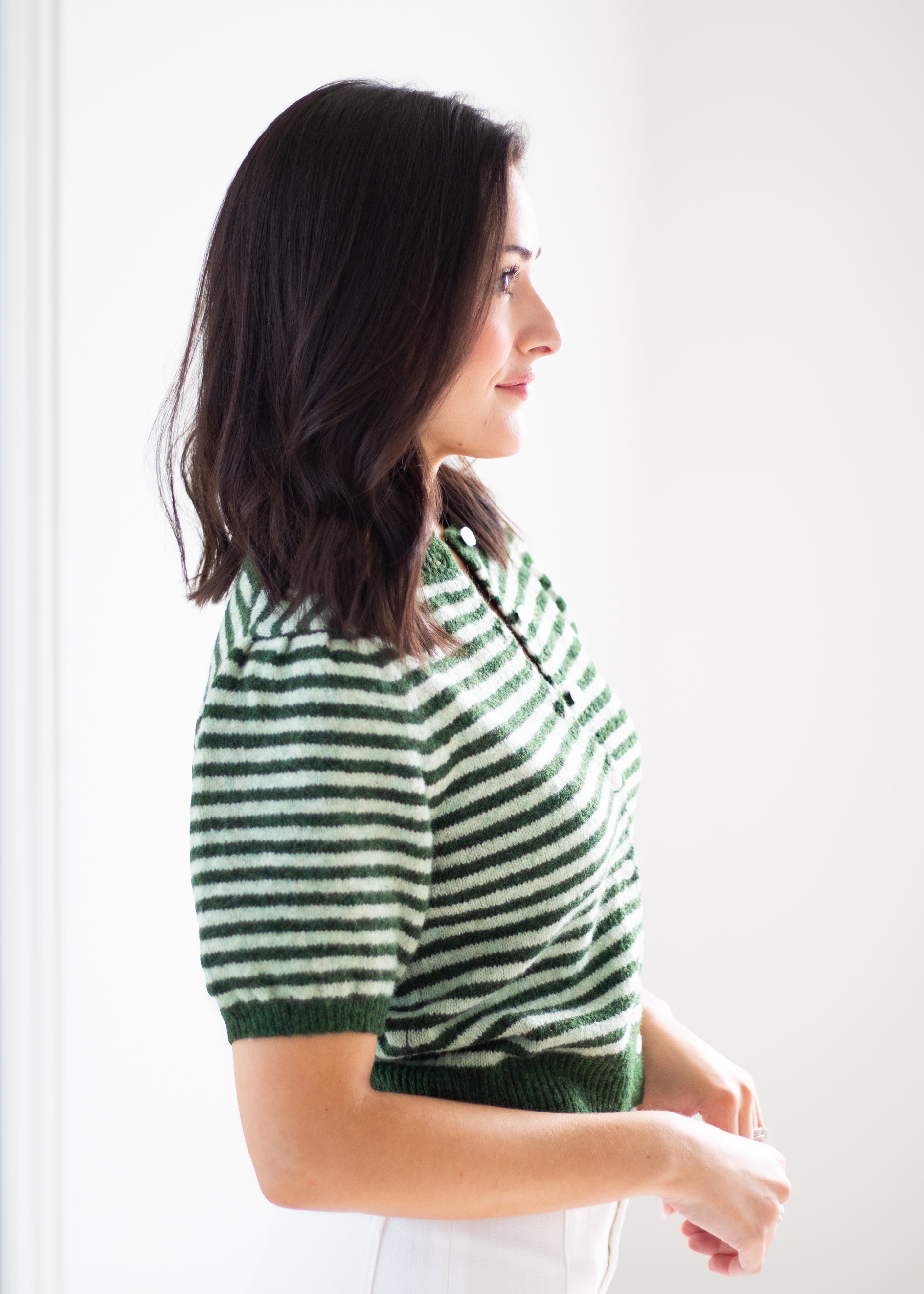 A woman in side profile wearing a green and white striped short-sleeve knit top against a bright white background.