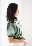 A woman in side profile wearing a green and white striped short-sleeve knit top against a bright white background.