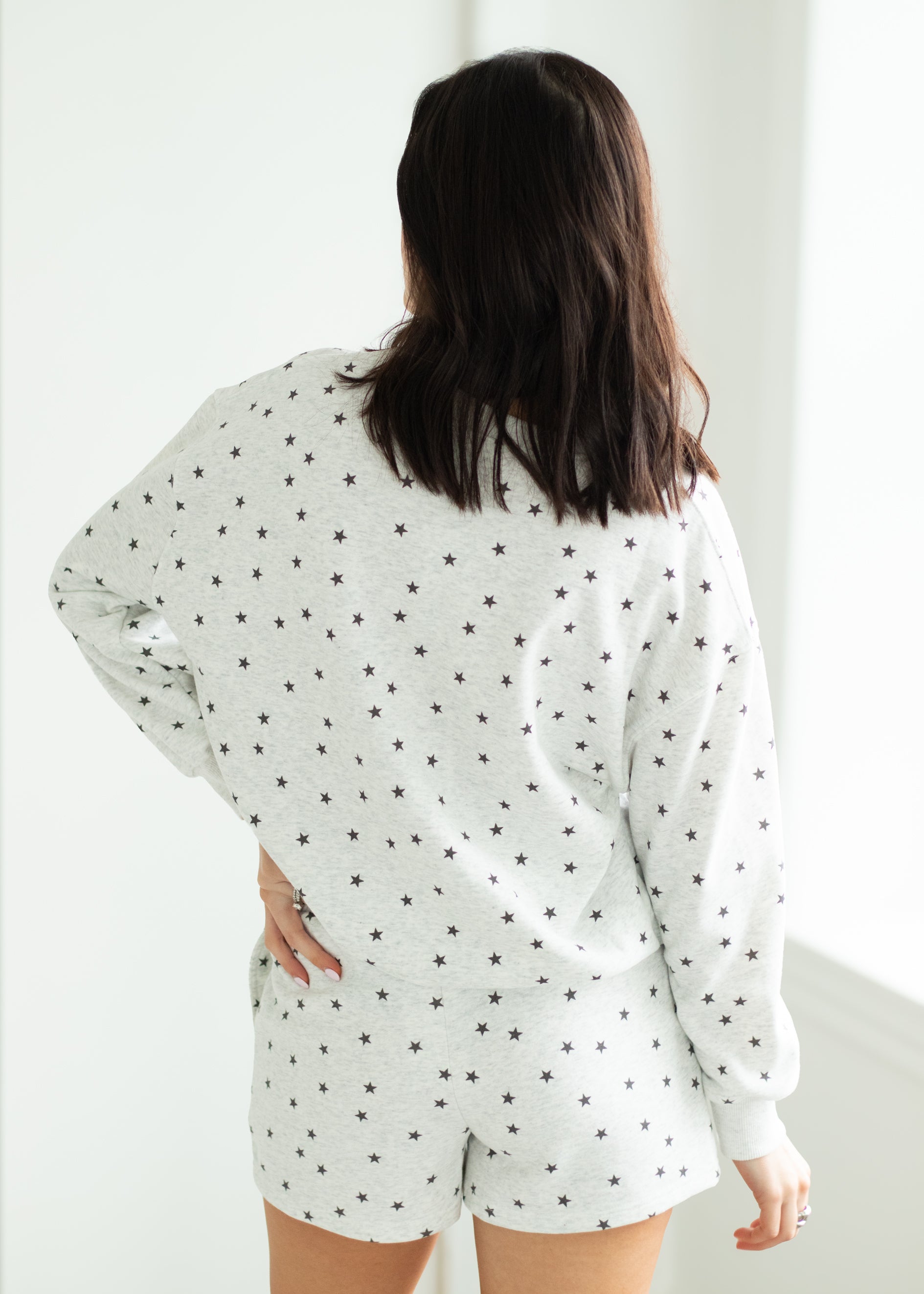 Woman wearing a white outfit with black stars in a minimalistic room.