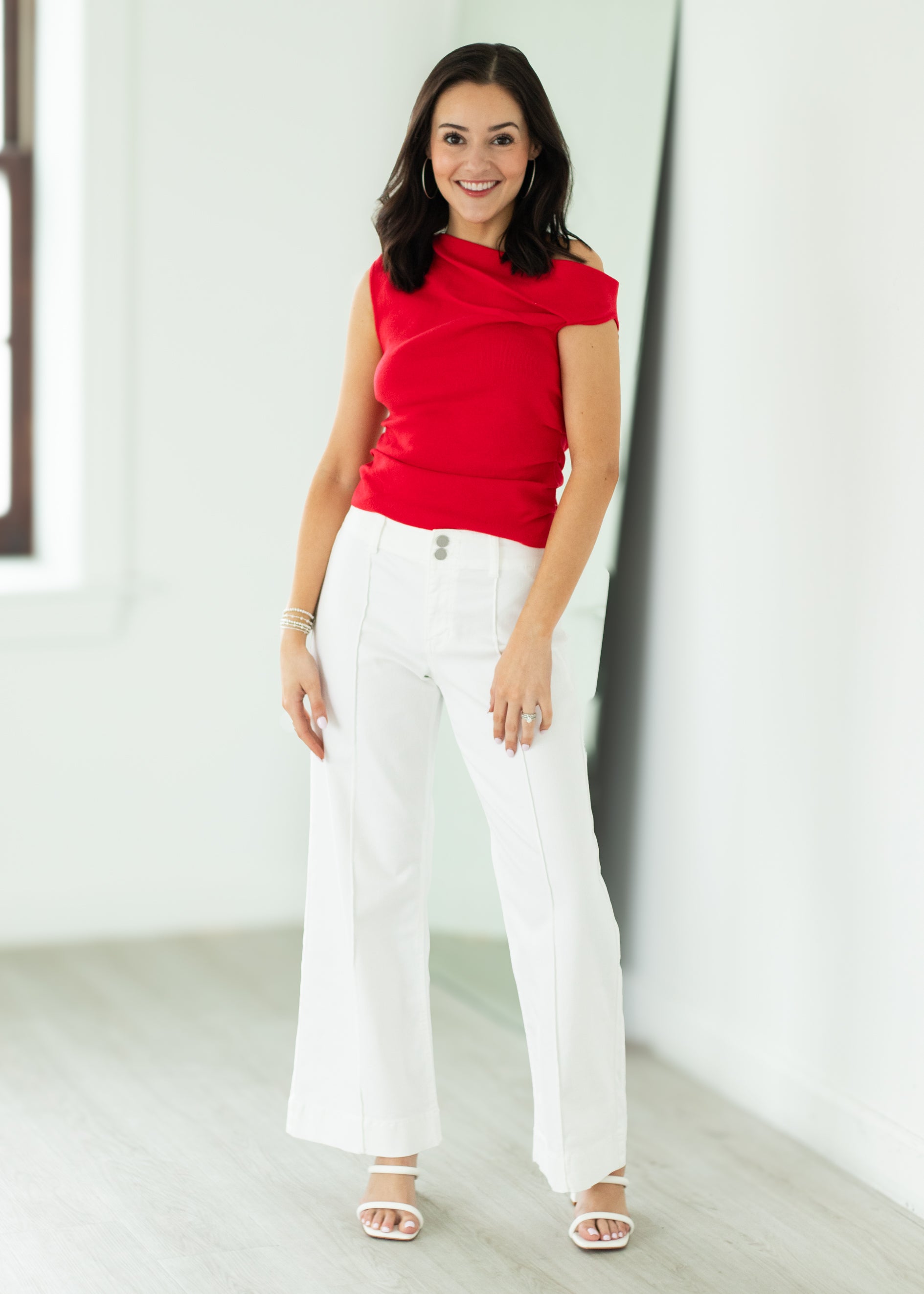 Woman wearing a red top and white pants in a minimal indoor setting