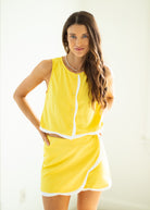 Woman wearing a yellow outfit with white trim on a plain background