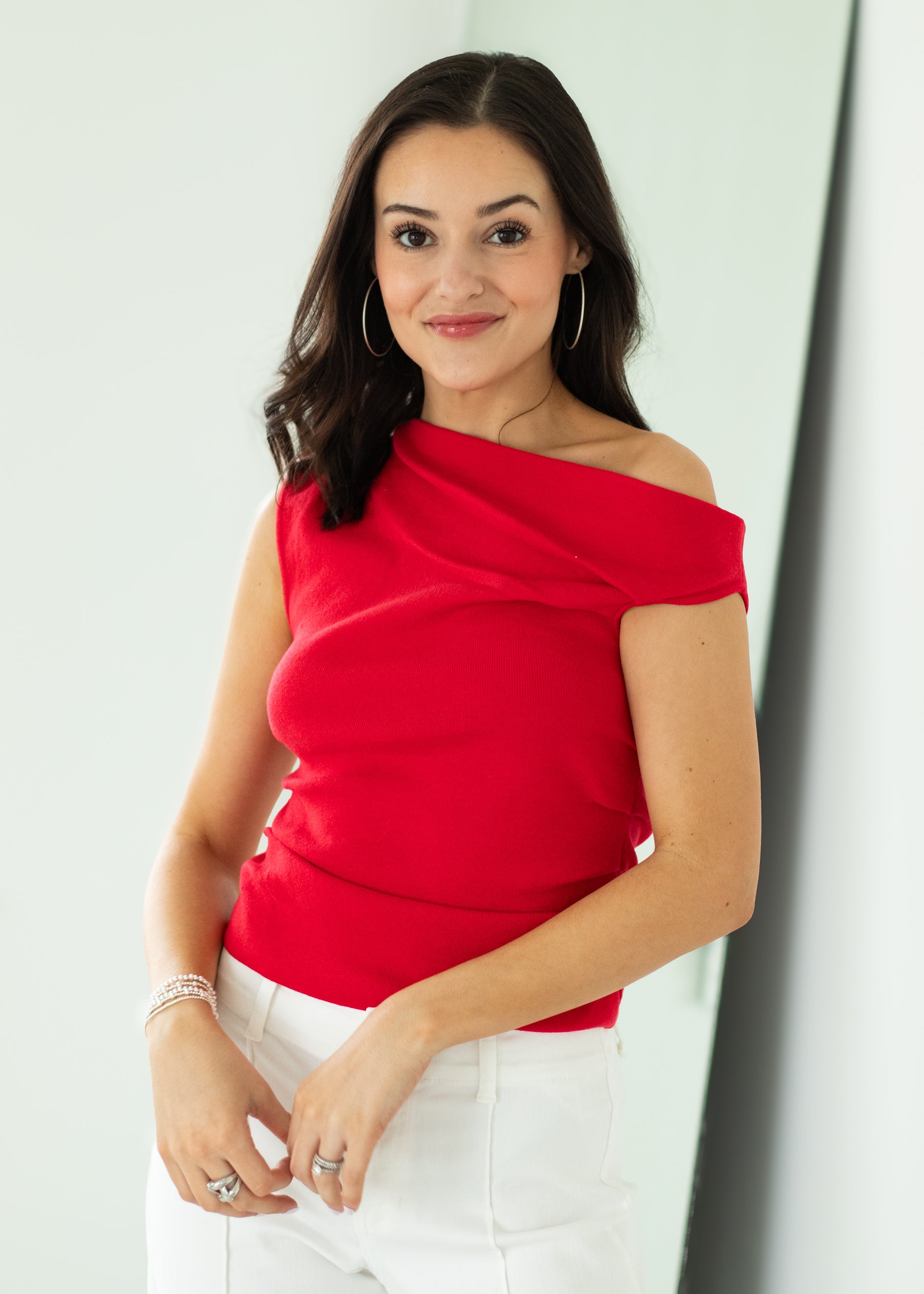 Woman wearing a red off-shoulder top and white pants against a light background