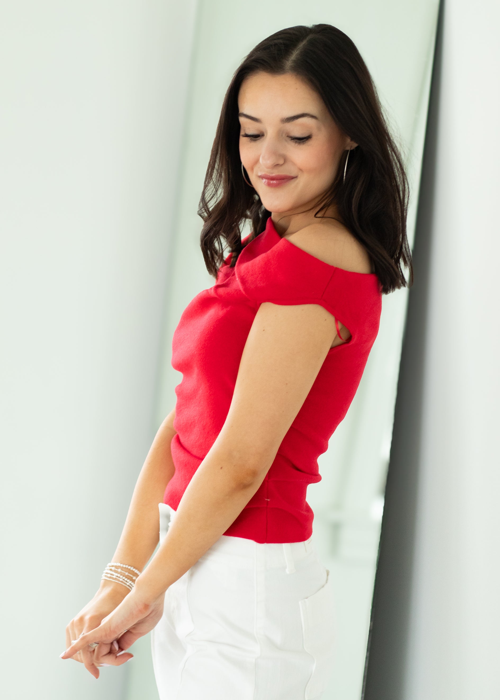 Woman wearing a red top and white pants against a light background